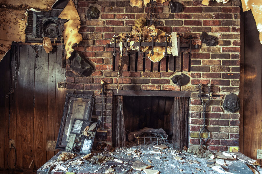  Image of a fireplace with damaged brick wall and mantle.