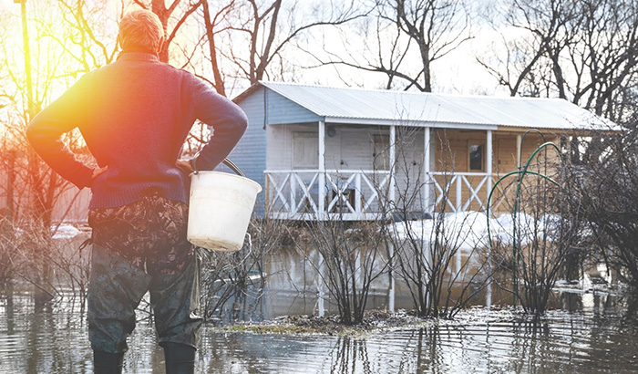 man-standing-in-flooded-area-holding-a-bucket-during-spring-flood,-emphasizing-flood-preparedness