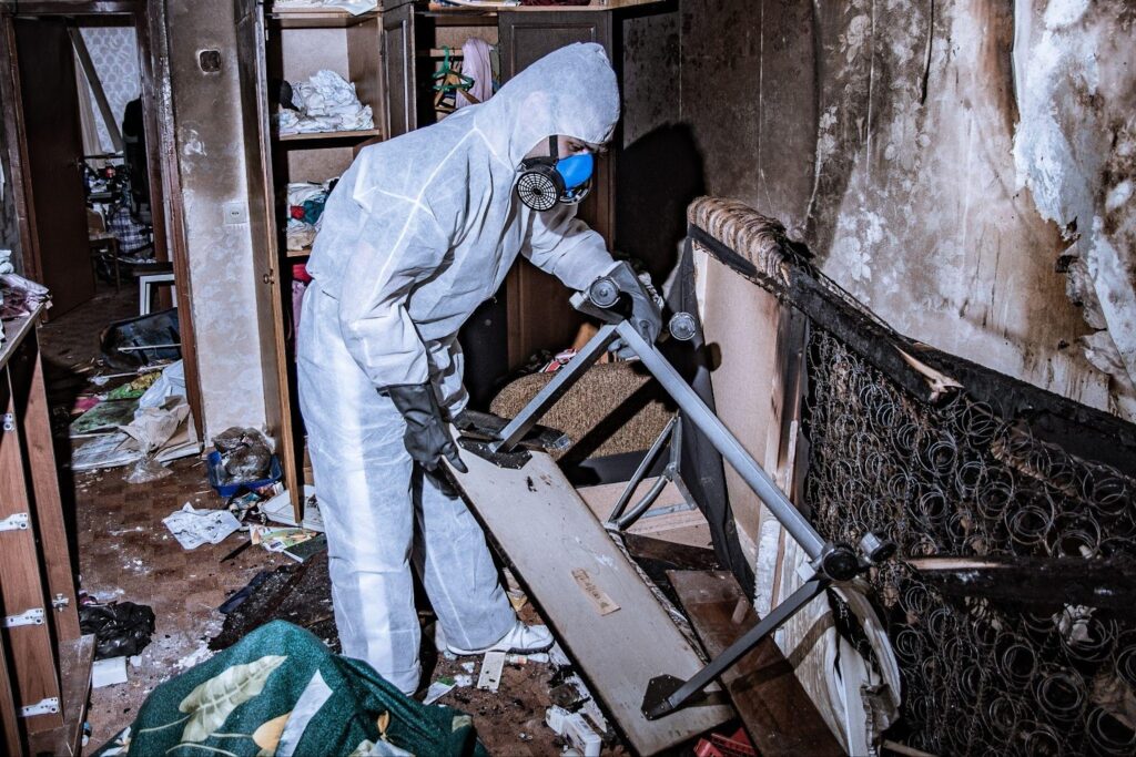 A man in a white suit and protective gear cleaning up a room, ensuring cleanliness and safety.
