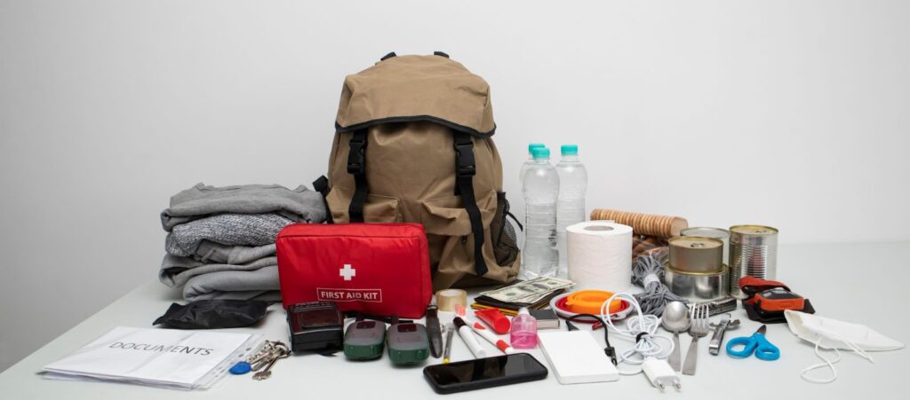 A disaster preparedness kit including a backpack, cell phone, water bottle, knife, flashlight, first aid kit, and other essential items.