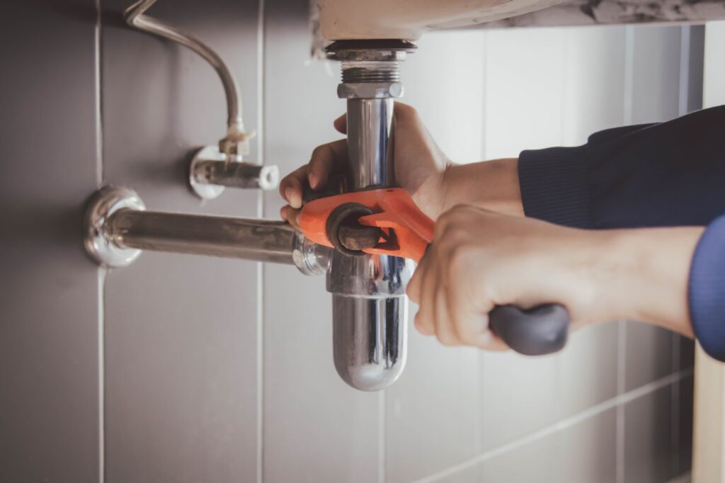 A person using a wrench to fix an aging pipe, addressing pipe replacement and water damage.