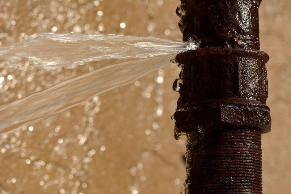 Close-up of water flowing from aging pipe, highlighting need for replacement due to water damage.