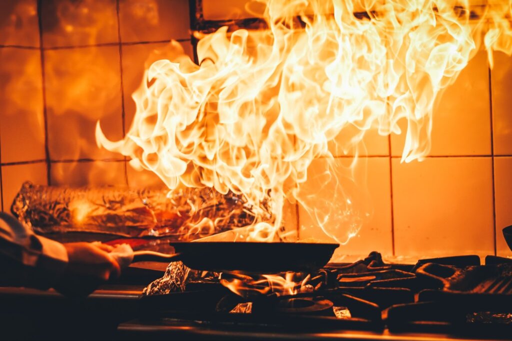 Kitchen fire with a person cooking on a stove with flames.