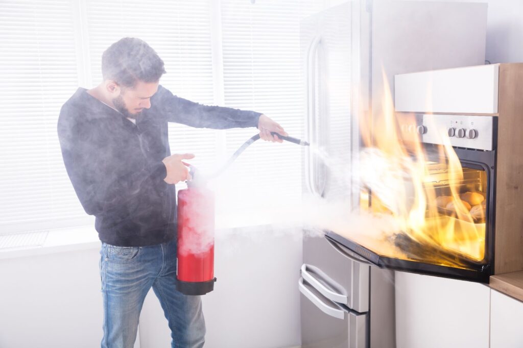 Man using fire extinguisher to put out kitchen fire, preventing fire and water damage.