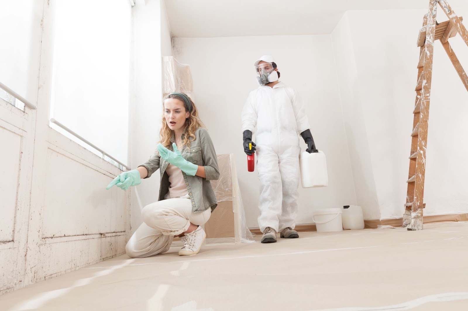 A man and woman in protective gear are painting a room, ensuring safety during mold remediation and removal efforts.