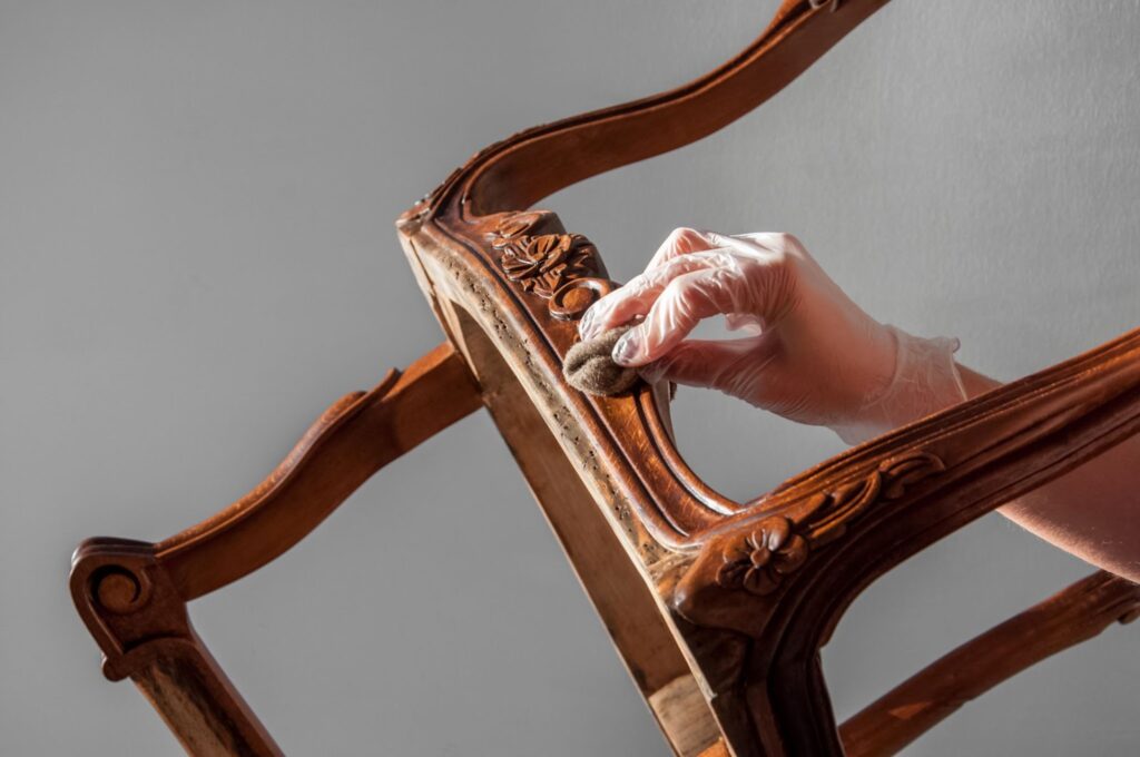 A person in gloves carefully cleans a water-damaged wooden chair, focusing on restoring its original condition.