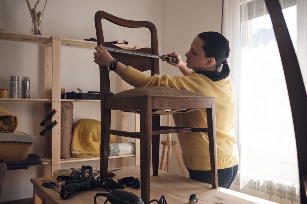 A woman sits on a chair in a room, focused on restoring water-damaged wood furniture with visible signs of damage.