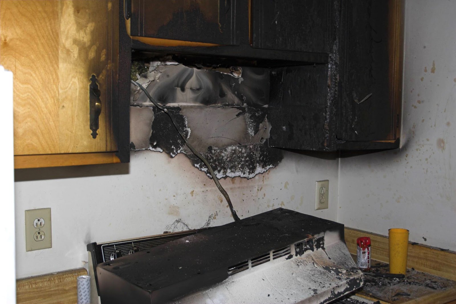 A black kitchen featuring a stove and cabinets, showcasing the aftermath of fire damage and the need for repair and cleanup.